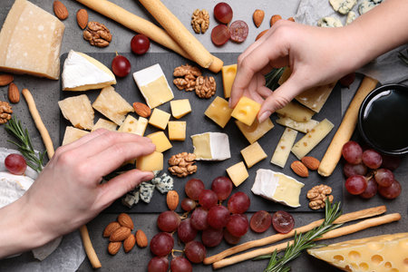 Women taking pieces from cheese plate on dark table, top viewの写真素材