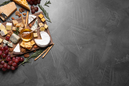 Cheese plate with honey, grapes and nuts on gray table, flat lay, Space for text