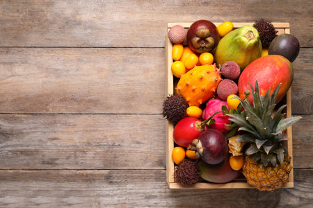 Crate with different exotic fruits on wooden table, top view. Space for textの写真素材