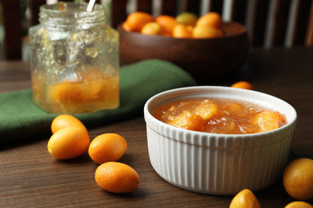 Delicious kumquat jam in bowl and fresh fruits on wooden tableの写真素材