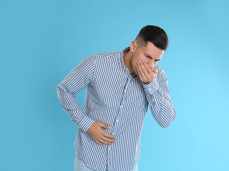 Man suffering from stomach ache and nausea on light blue background. food poisoningの写真素材