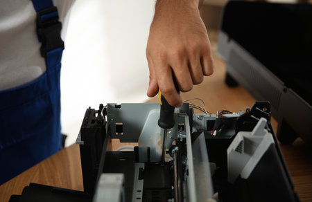 Repairman with screwdriver fixing modern printer indoors, closeupの写真素材