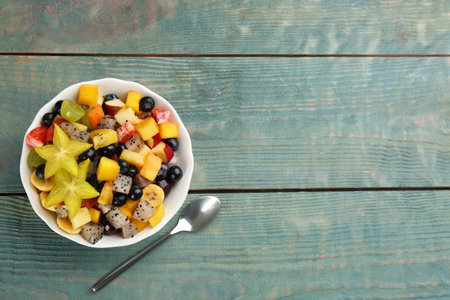 Delicious exotic fruit salad and spoon on light blue wooden table, flat lay. Space for textの写真素材