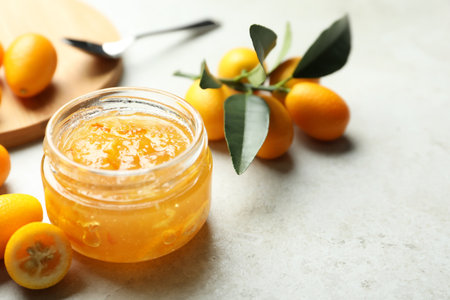 Delicious kumquat jam in jar and fresh fruits on light gray table, space for textの写真素材