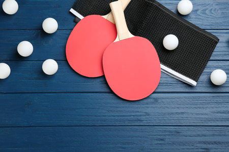 Table tennis rackets, net and balls on blue wooden table, flat lay. Space for textの写真素材
