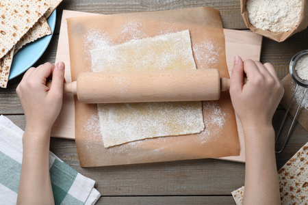 Woman rolling raw dough for traditional matzo at wooden table, top viewの写真素材
