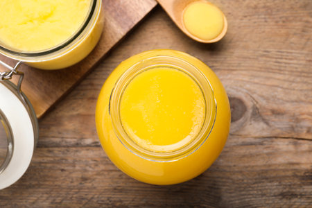 Glass jars and spoon of Ghee butter on wooden table, flat lay