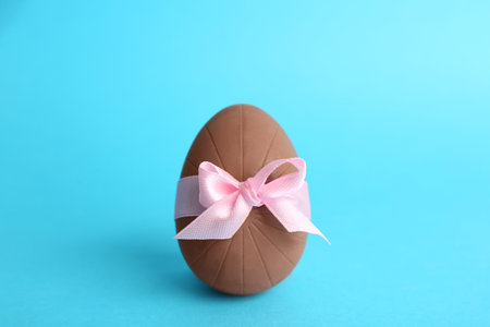 Sweet chocolate egg with pink bow on light blue backgroundの写真素材