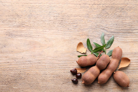 Ripe tamarinds and fresh leaves on wooden table, flat lay. Space for textの写真素材