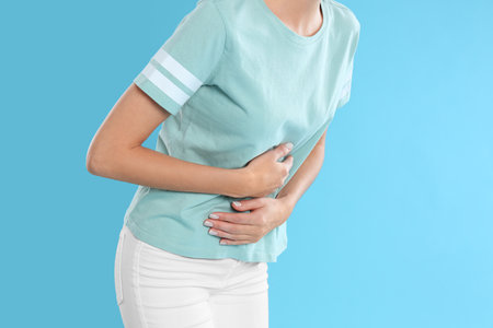 Woman suffering from stomach ache on light blue background, closeup. food poisoningの写真素材