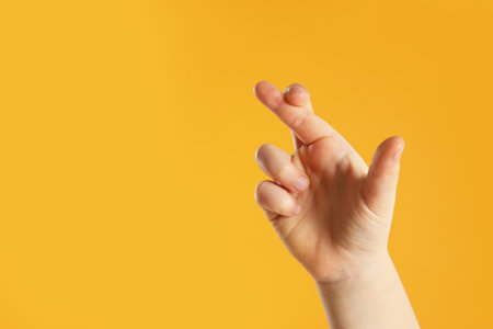 Child holding fingers crossed on yellow background, closeup with space for text. good luck superstitionの写真素材