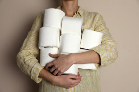 Woman with heap of toilet paper rolls on beige background, closeupの写真素材