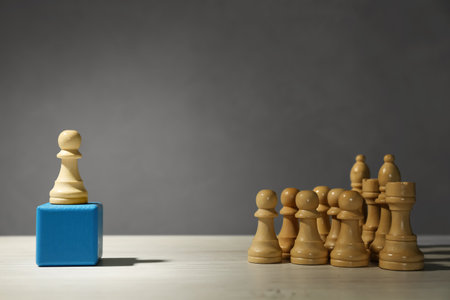 White chess piece standing out from others on wooden table against gray backgroundの写真素材
