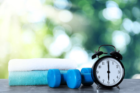 Alarm clock, towels and dumbbells on marble table outdoors. morning exerciseの写真素材