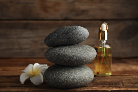 Stack of gray spa stones, flower and oil on wooden tableの写真素材