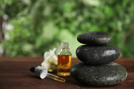 Stack of gray spa stones, oil and flower on wooden table outdoors, space copy textの写真素材