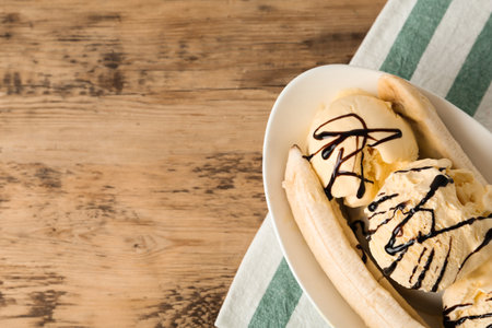 Delicious banana split ice cream with chocolate topping on wooden table, top view. Space for textの写真素材