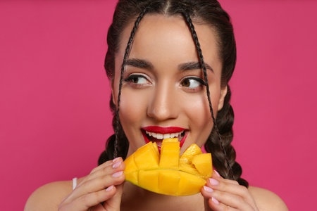 Young woman eating fresh mango on pink background. Exotic fruitの写真素材