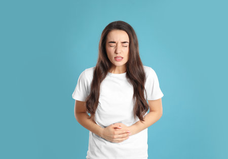 Young woman suffering from stomach ache on light blue background. Food poisoningの写真素材