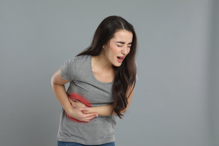 Young woman suffering from liver pain on grey backgroundの写真素材