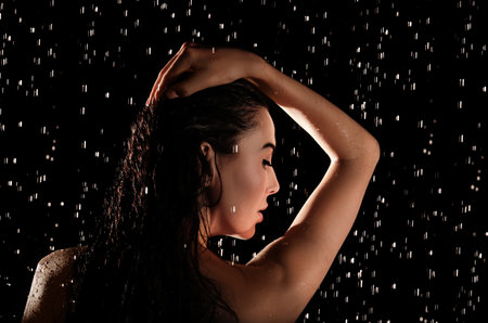 Young woman washing hair while taking shower on black backgroundの写真素材