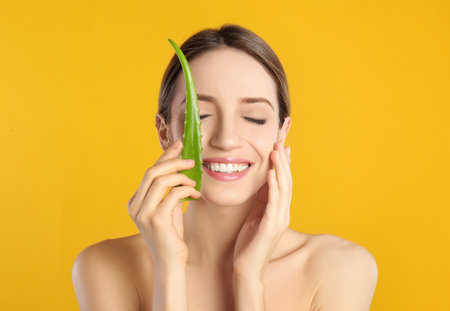 Happy young woman with aloe leaf on yellow backgroundの写真素材