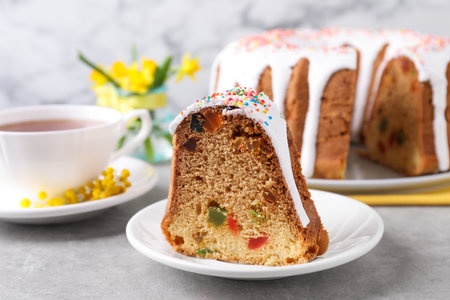 Piece of glazed Easter cake with sprinkles and candied fruits on gray table, closeup