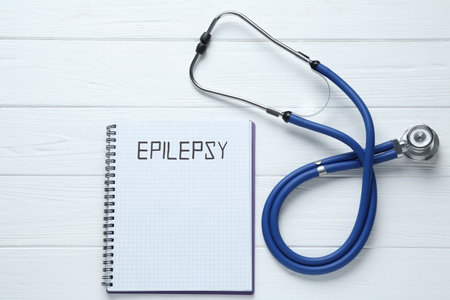 Notebook with word Epilepsy and stethoscope on white wooden table, flat layの写真素材