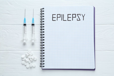 Notebook with word Epilepsy, pills and syringes on white wooden table, flat layの写真素材