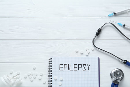 Notebook with word Epilepsy, stethoscope, pills and syringes on white wooden table, flat lay. Space for textの写真素材