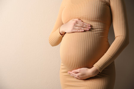 Pregnant woman touching her belly on beige background, closeupの写真素材