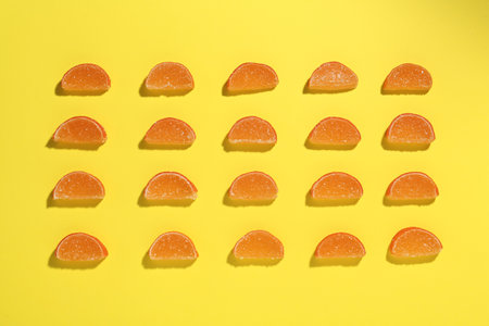 Delicious orange marmalade candies on yellow background, flat layの写真素材