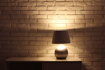 Stylish glowing night lamp on table near white brick wall. Space for textの写真素材