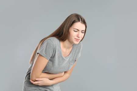 Woman suffering from stomach ache on gray background, space for text. food poisoningの写真素材