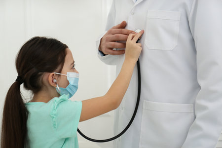 Little girl playing with pediatrician during visit in hospital. Patient wearing protective maskの写真素材