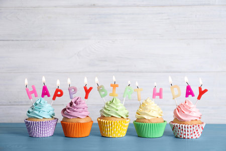 Birthday cupcakes with burning candles on blue wooden tableの写真素材