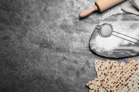 Traditional matzos, rolling pin and flour on gray table, flat lay. Space for text