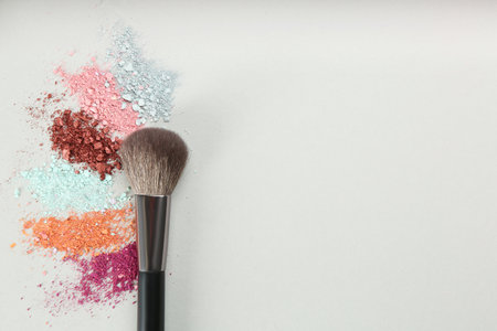 Makeup brush and scattered eye shadows on light gray background, flat lay. Space for textの写真素材