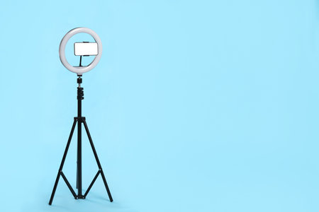 Modern tripod with ring light and smartphone on light blue background. Space for textの写真素材