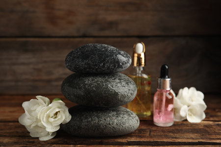 Stack of gray spa stones, flowers and oils on wooden tableの写真素材