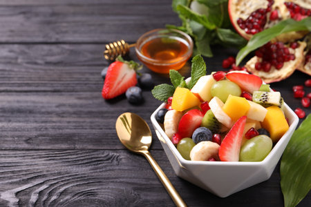 Delicious fresh fruit salad in bowl on black wooden table, space for textの写真素材