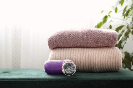 Modern fabric shaver and woolen sweaters on green bench indoors, space for textの写真素材