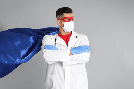Doctor wearing face mask and cape on gray background. Super hero power for medicineの写真素材