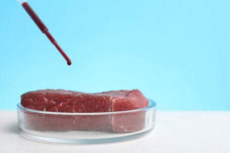 Dripping red liquid onto sample of lab grown meat on white table. Space for textの写真素材