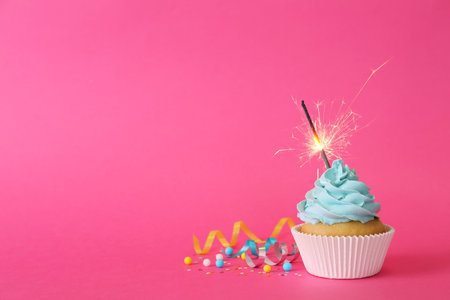 Birthday cupcake with burning sparkler and streamers on pink background. Space for textの写真素材