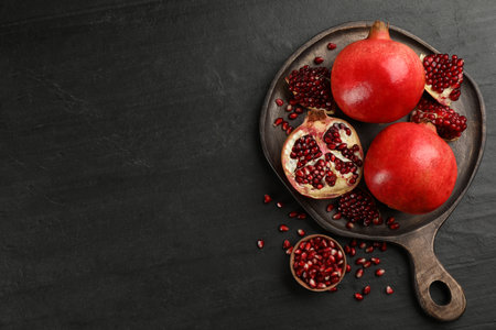Delicious ripe pomegranates on black table, flat lay. Space for textの写真素材