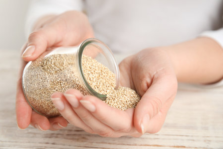 Woman with jar of white quinoa at wooden table, closeupの写真素材