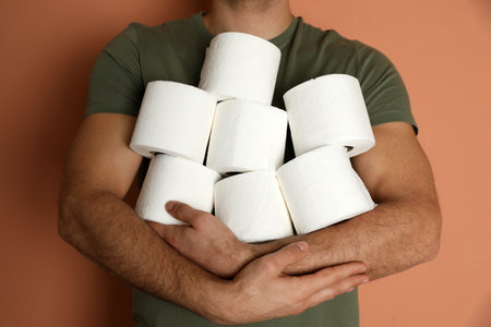 Man with heap of toilet paper rolls on brown background, closeupの写真素材