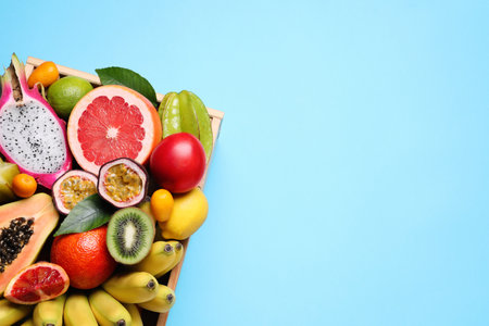 Crate with different exotic fruits on light blue background, top view. Space for textの写真素材