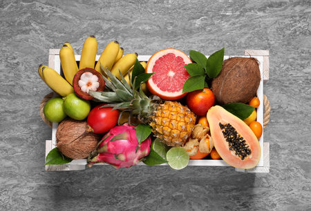 Different tropical fruits in wooden box on gray background, top viewの写真素材